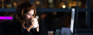 Woman drinking coffee as she works on the computer at night