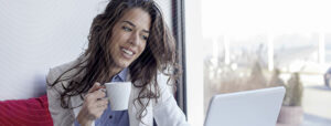 woman smiling drinking coffee and using laptop