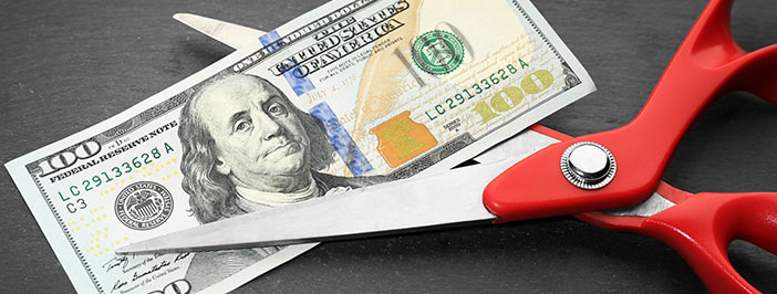 Red scissors cutting money to signify cut IT costs.